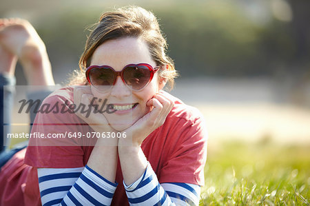 Portrait of young woman wearing heart shape sunglasses lying on grass