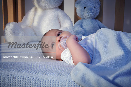 Baby boy and teddy bears in crib at night