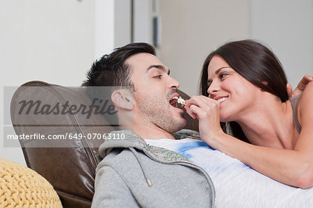 Young couple lying on sofa sharing popcorn Young couple lying on sofa sharing popcorn