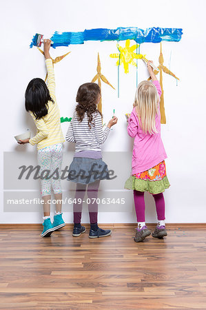 Three girls painting wind turbines on wall