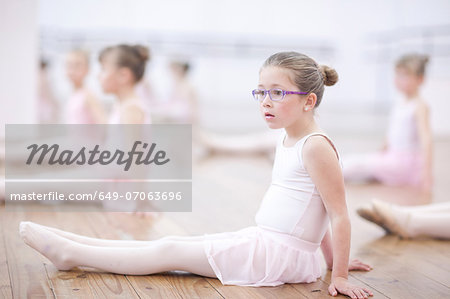 Distracted young ballerina sitting on floor