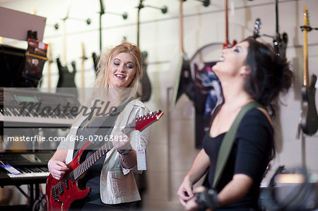 Two young women trying electric guitars in music store