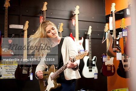 Young woman testing guitar in music store