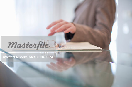 Young female picking up eyeglasses from reception desk