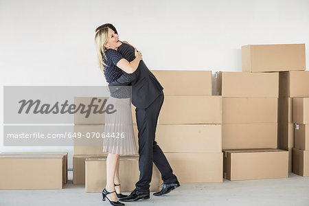 Businessman and -woman hugging in front of stack of cardboard boxes