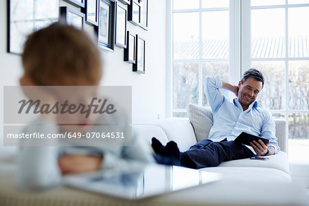 Father and son sitting on sofa using digital tablets