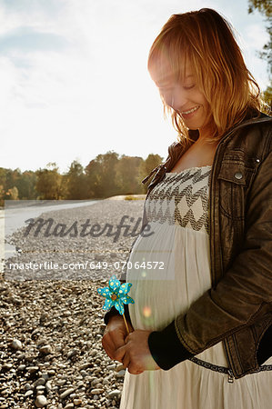 Pregnant woman standing beside river holding windmill