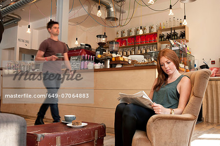 Young woman having tea and reading newspaper in cafe