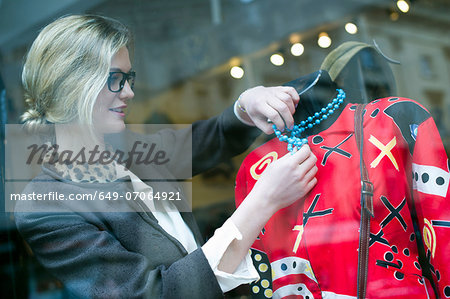 Woman putting necklace on shop dummy