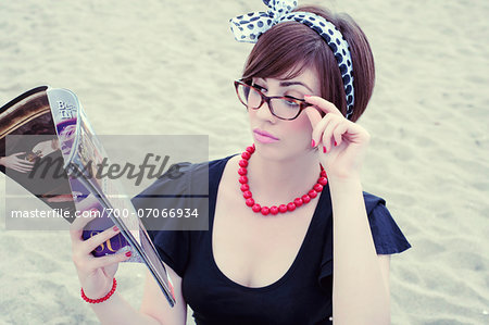 Portrait of young woman wearing horn-rimmed eyeglasses reading magazine on beach, Italy