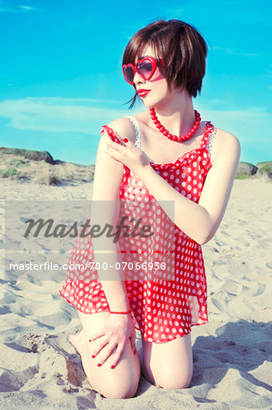 Young woman kneeling in sand on beach, wearing retro clothing, Italy