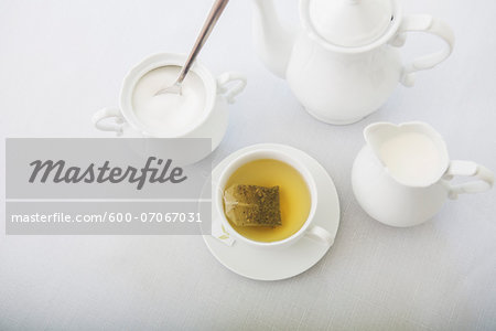 Cup of tea in porcelain white teacup with saucer, sugar bowl, creamer and teapot, studio shot Cup of tea in porcelain white teacup with saucer, sugar bowl, creamer and teapot, studio shot