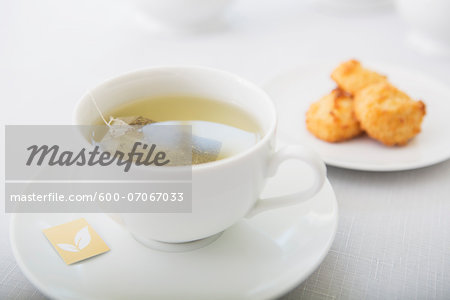 Cup of tea in porcelain white teacup with saucer and plate of coconut macaroons, studio shot Cup of tea in porcelain white teacup with saucer and plate of coconut macaroons, studio shot