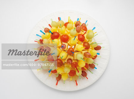 Appetizer picks with cheese and fruit displayed in a ball shape on paper plate, on white background, studio shot