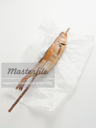 Fried mackerel pike fish on stick, on paper wrapper, studio shot