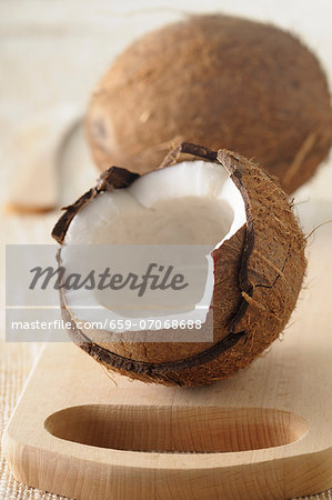 A whole coconut and one broken open, on a wooden board