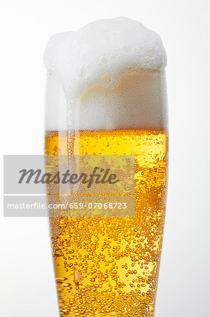 A glass of light beer with overflowing beer foam A glass of light beer with overflowing beer foam