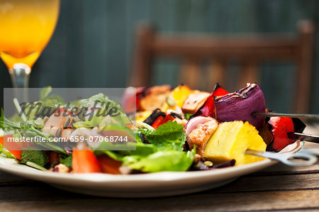 Barbecued chicken kebabs with a side salad on a garden table