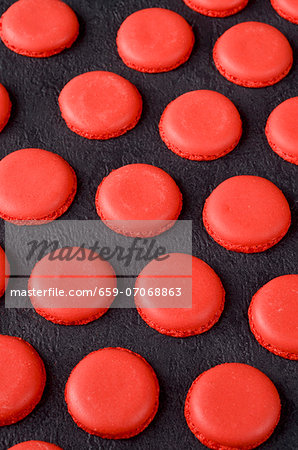 Freshly baked red macaroon halves on a slate surface