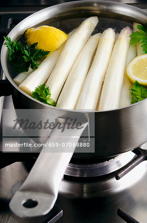 Peeled white asparagus in a saucepan with lemon and parsley