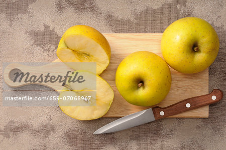 Golden Delicious apples, whole and halved, on a chopping board