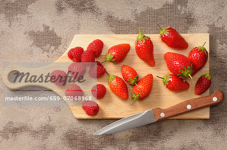 Fresh strawberries and raspberries on a chopping board with a knife Fresh strawberries and raspberries on a chopping board with a knife