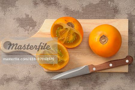 Fresh naranjillas on a chopping board with a knife