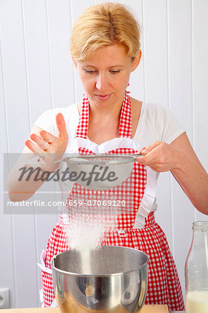 A woman sieving flour into a mixing bowl