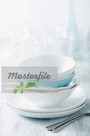 Stacked dinner bowls and plates, drinking glasses and forks