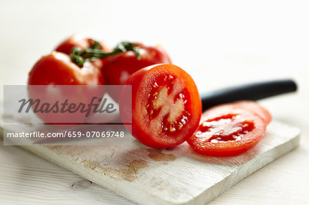 Sliced tomatoes and whole tomatoes on a board with a knife