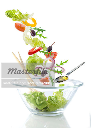 Salad ingredients falling into a glass bowl