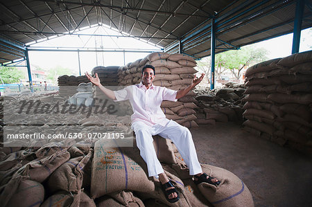 Man sitting on stack of wheat sacks in a warehouse, Anaj Mandi, Sohna, Gurgaon, Haryana, India