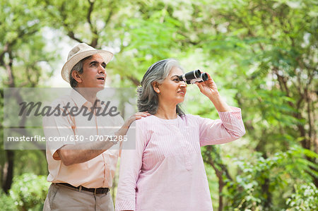 Woman looking through binoculars with her husband standing behind her, Lodi Gardens, New Delhi, India