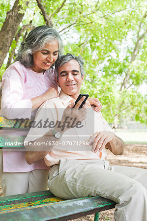 Mature couple looking at a mobile phone and smiling, Lodi Gardens, New Delhi, India