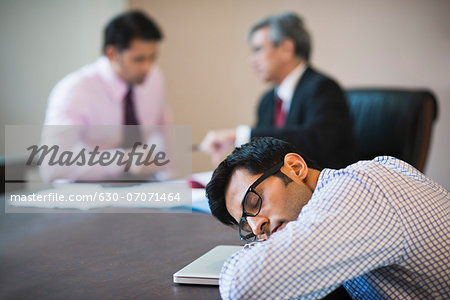 Businessman sleeping in a conference with two businessmen in the background