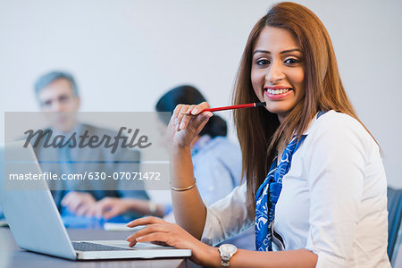 Portrait of a businesswoman working on a laptop with her colleagues discussing in the background