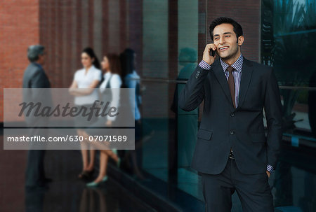 Businessman talking on a mobile phone with their colleagues in the background