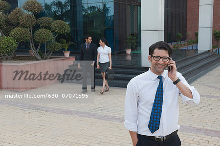 Businessman talking on a mobile phone with their colleagues in the background