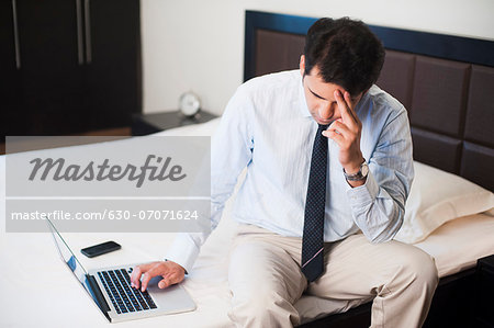 Worried businessman using a laptop on the bed