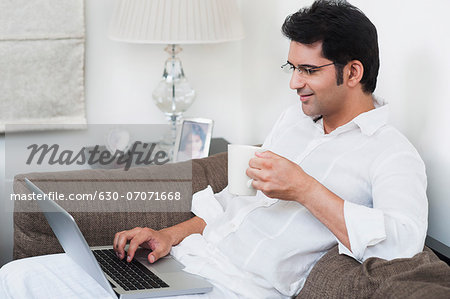 Man working on a laptop and holding a cup of coffee