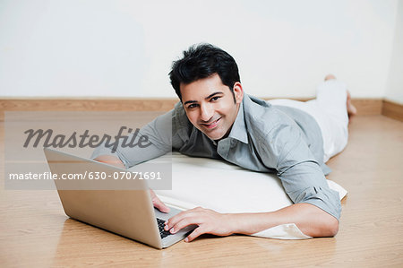 Man lying on a floor and working on a laptop