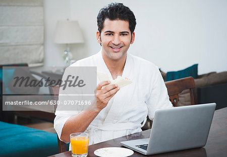 Businessman eating breakfast and working on a laptop