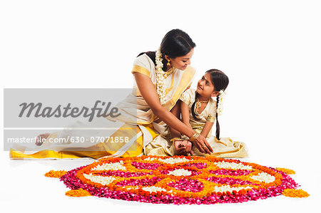 South Indian woman making a rangoli of flowers with her daughter at Onam