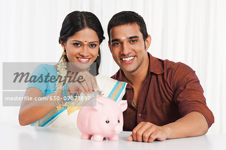 South Indian couple putting cash in a piggy bank