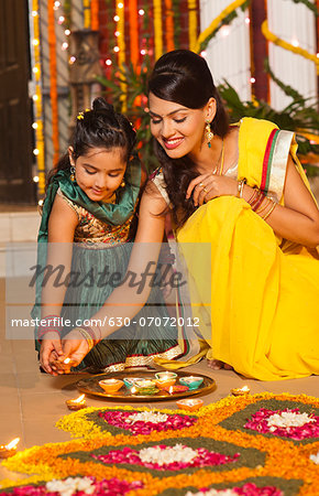 Woman and her daughter decorating rangoli with oil lamps on Diwali