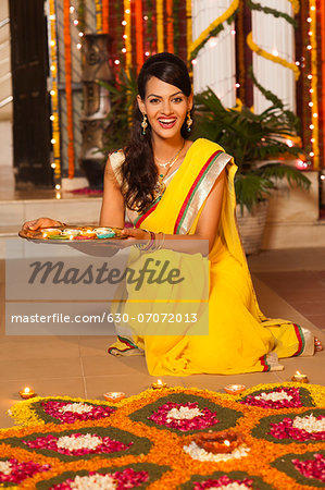 Woman decorating rangoli with oil lamps on Diwali