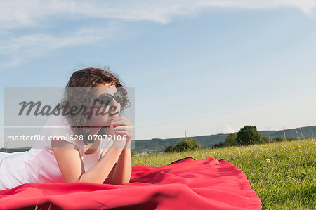 Girl with sunglasses lying on blanket in meadow