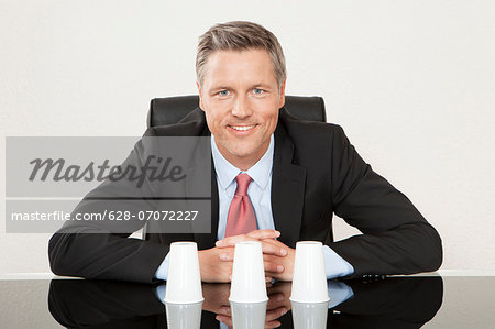 Businessman playing shell game with plastic cups at desk