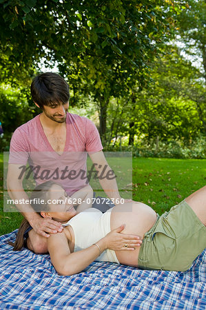 Man and pregnant woman on a blanket in a park