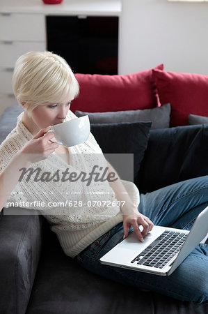 Young woman with cup using laptop on couch